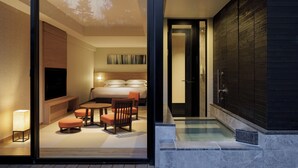Una habitación de hotel moderna con pared de vidrio, zona de estar con sofá y sillones, cama, televisor y pequeña piscina.