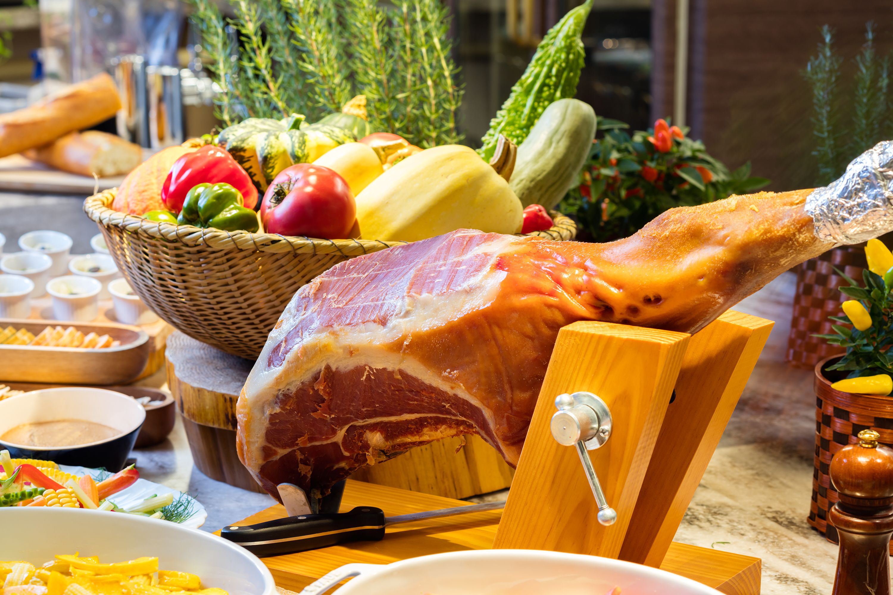 A large ham on a carving stand, surrounded by various vegetables and condiments.