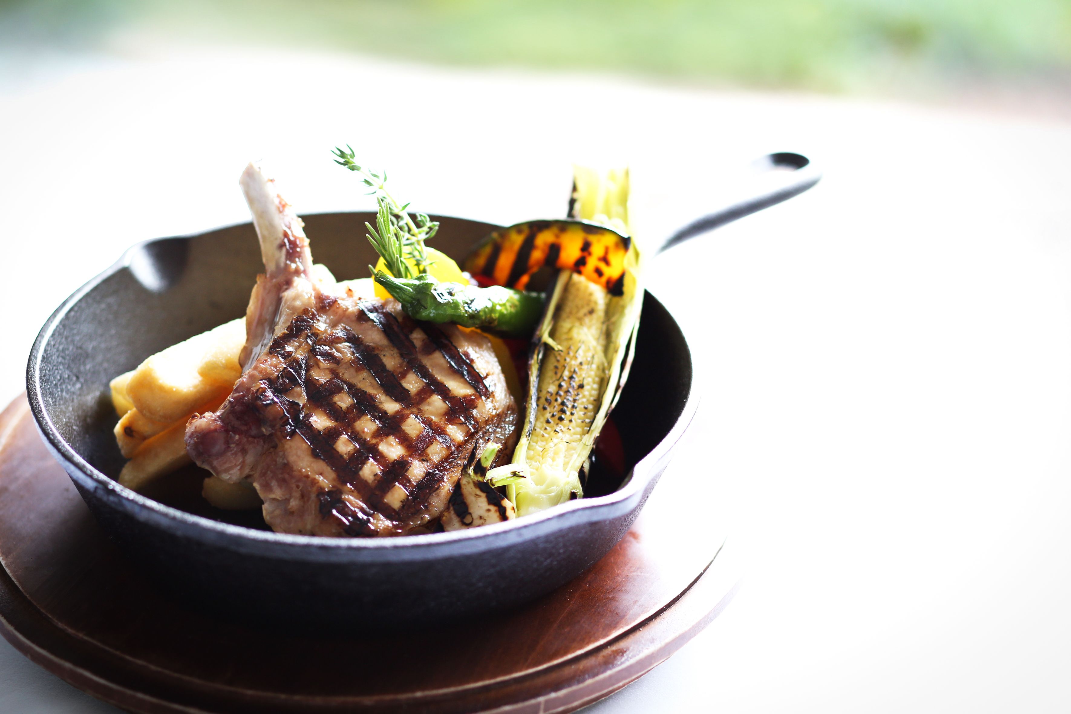 A skillet with grilled meat, vegetables, and a sprig of herb.
