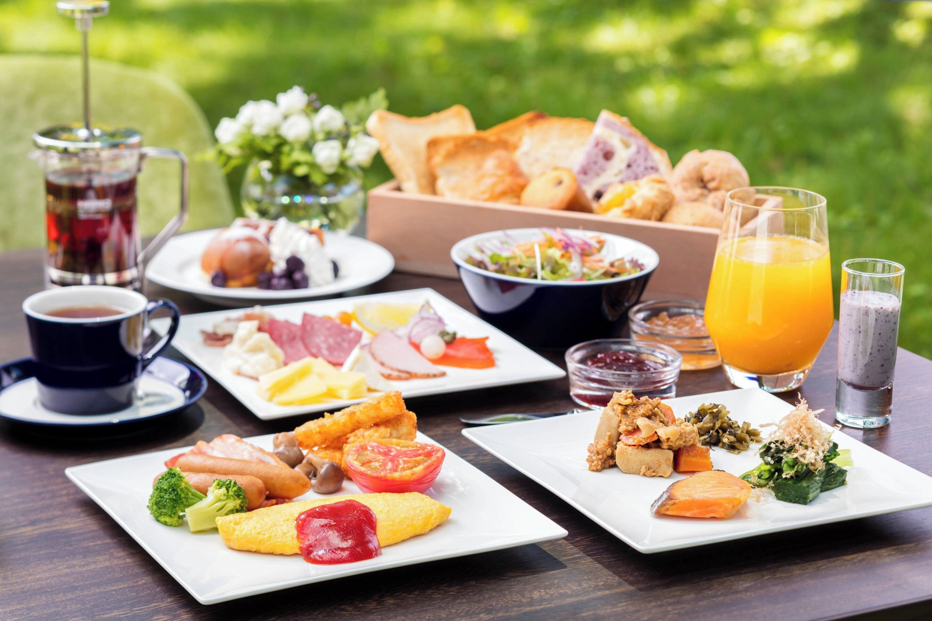 A breakfast buffet with various dishes, drinks, and a coffee setup on a wooden table.