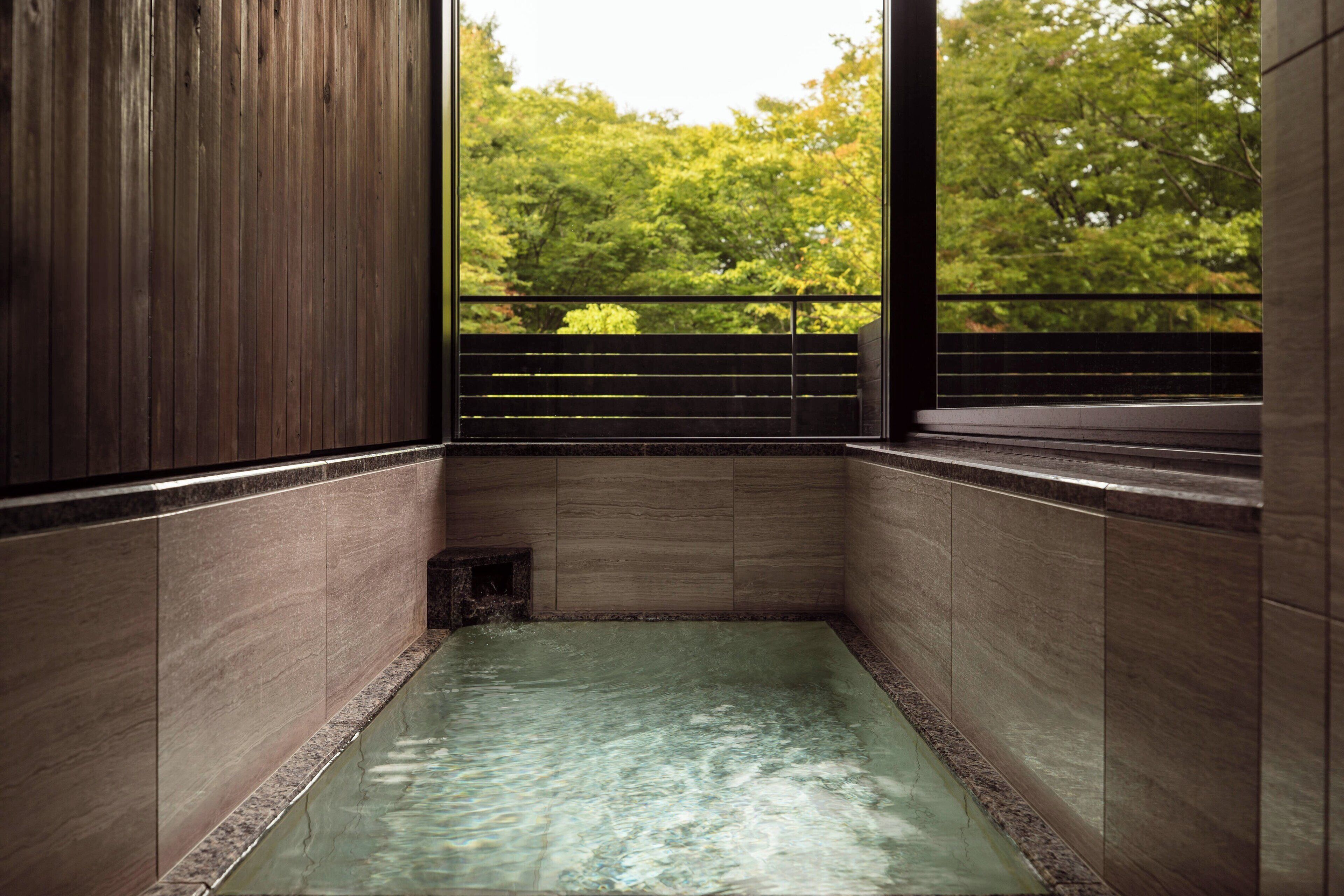 Un onsen japonais traditionnel, avec un intérieur en bois, un sol carrelé et une vue sur une végétation luxuriante.