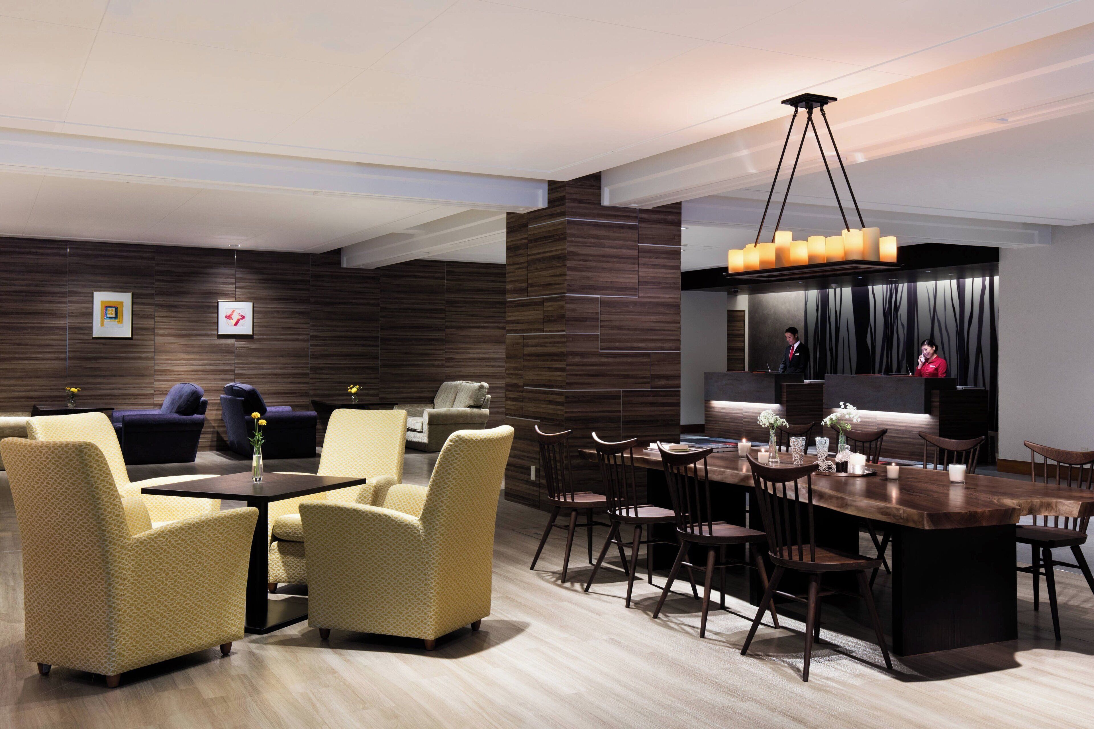 A modern hotel lobby with a dining area, sofas, and a bar.