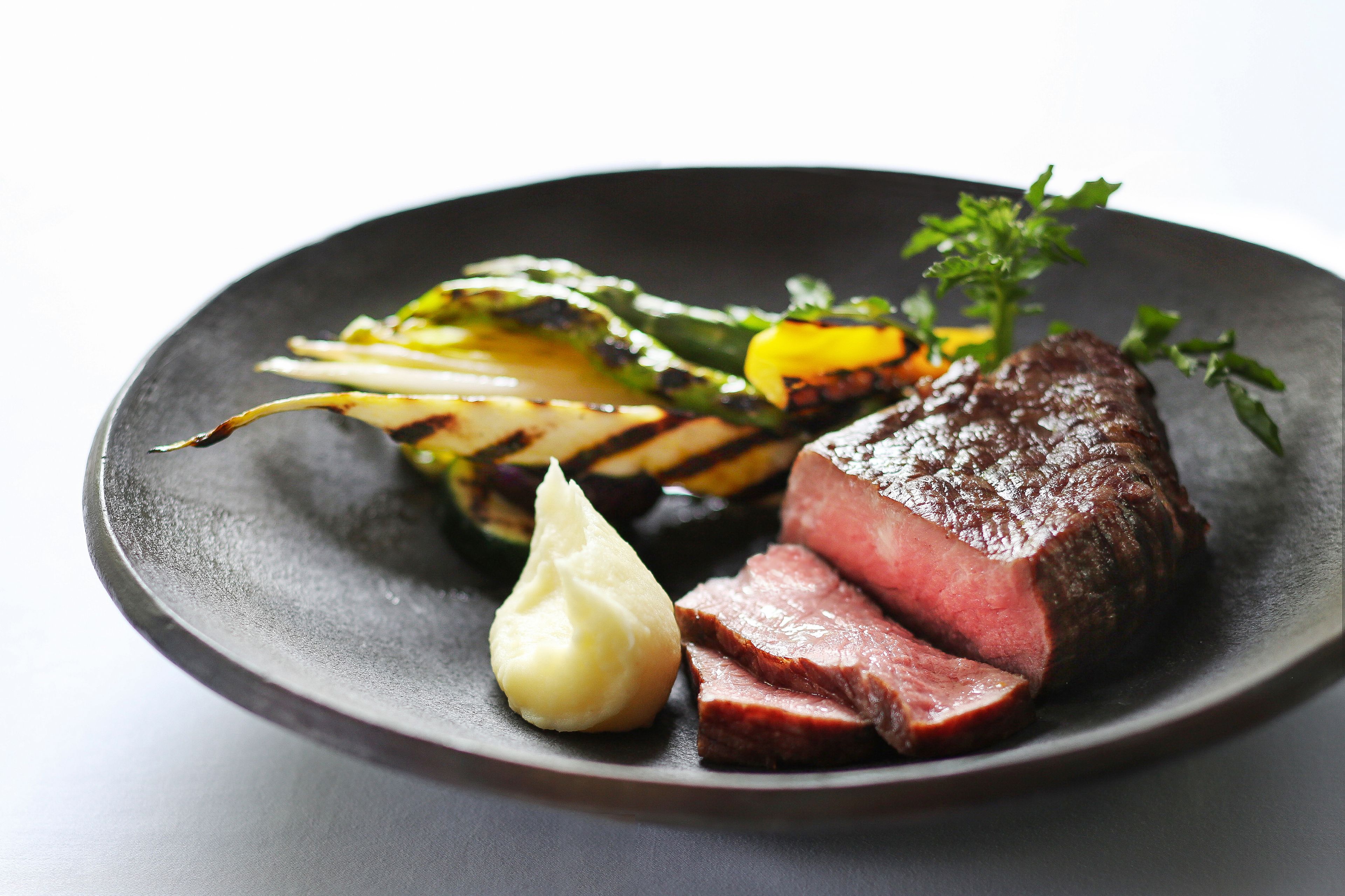 A plate with steak, grilled vegetables, and a dollop of sauce.