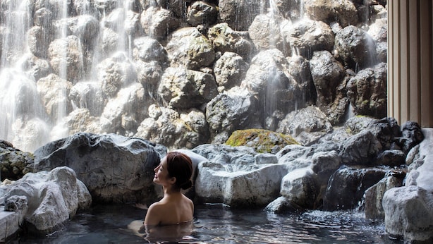Una persona en un manantial termal rodeada de rocas grandes y una cascada.