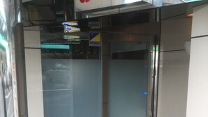 A glass elevator door with a security sign, a tiled floor, and a small mat at the entrance. - Que Sera Sera - Adults Only (Neyagawa)