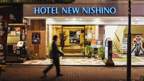 The entrance of Hotel New Nishino with a clear sign, a potted plant, and a poster on the wall.
