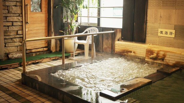A hot spring bath area with a wooden door, a white plastic chair, and a sign in a foreign language. - Hotel New Nishino (Kagoshima)
