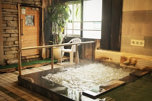 Zona de baño con aguas termales, una puerta de madera, una silla de plástico blanco y un letrero en un idioma extranjero.
