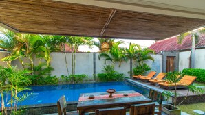 Zona junto a la piscina con mesa y sillas de madera, una piscina pequeña y sillones de descanso.