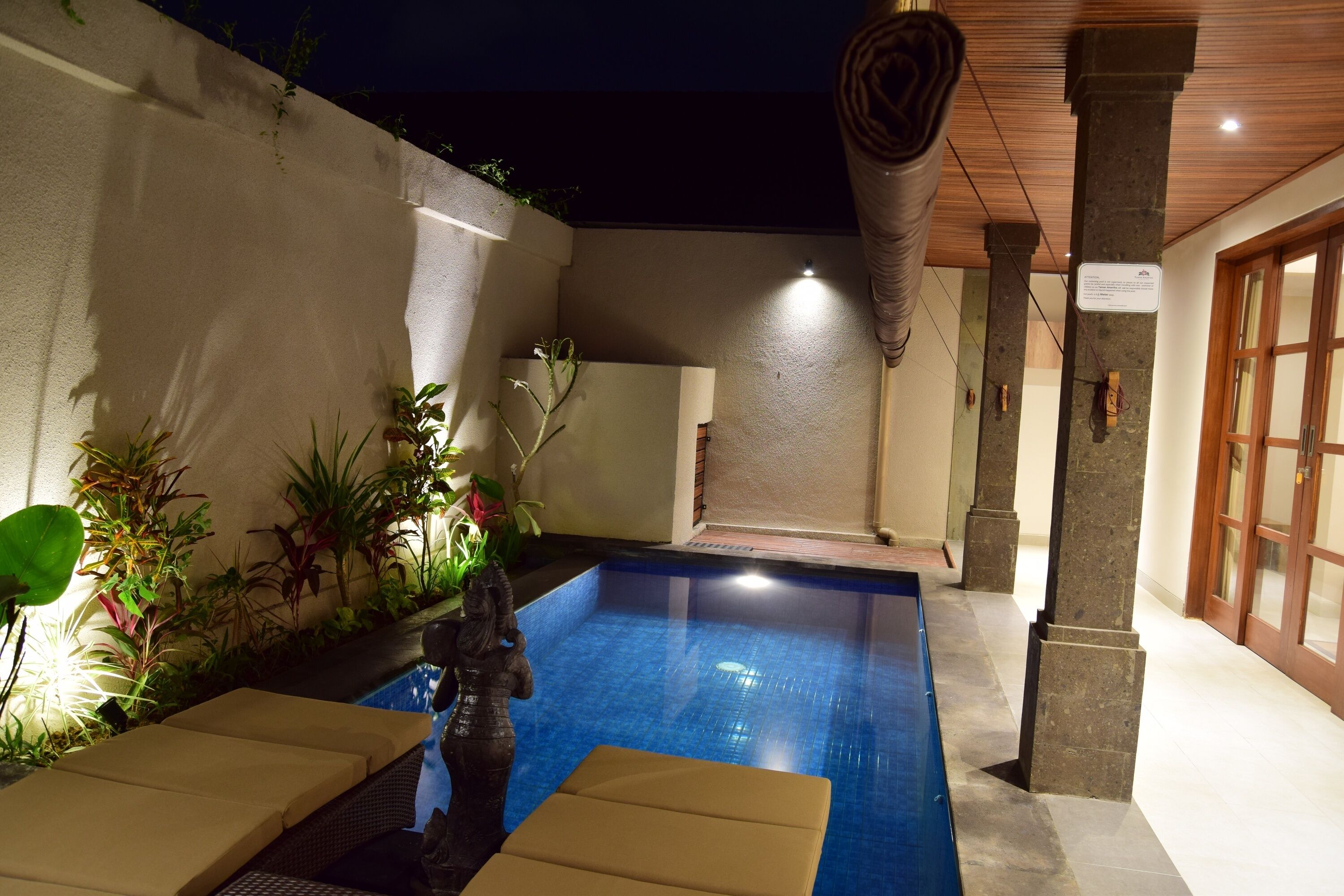 A swimming pool area with lounge chairs and a statue, surrounded by plants and a stone wall.