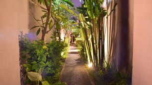 Un sendero estrecho bordeado por abundante vegetación y una pared, que conduce a una escalera.