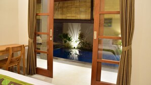 Una habitación con una mesa y sillas de madera, una puerta corrediza de vidrio que da a un jardín con fuente de agua y plantas.