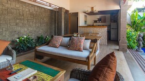 Un rincón exterior acogedor con sofá y sillones, una mesa de madera y una cocina al fondo.