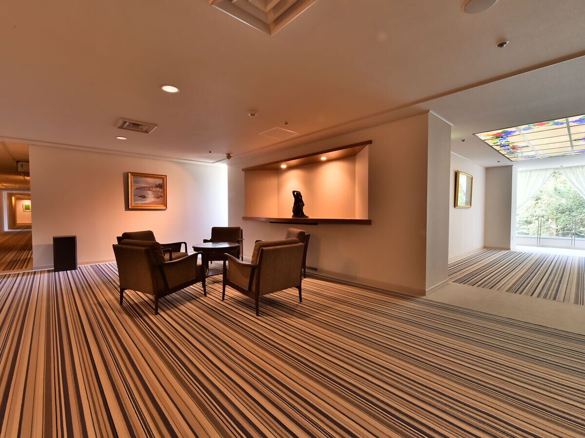 Un hall de hotel con alfombra a rayas, un mostrador de recepción y una estatua en la pared.