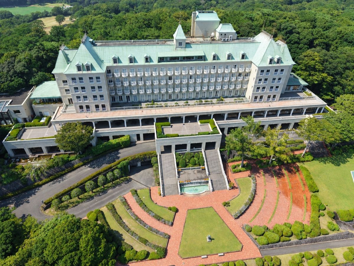 A large, multi-story hotel with a central courtyard, surrounded by lush greenery.