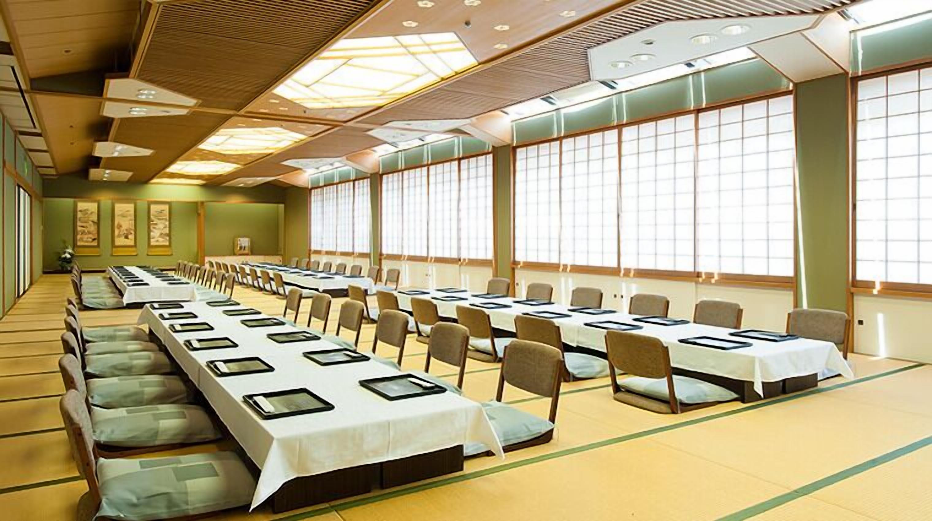 A conference room with long tables and chairs, large windows, and a high ceiling with skylights.