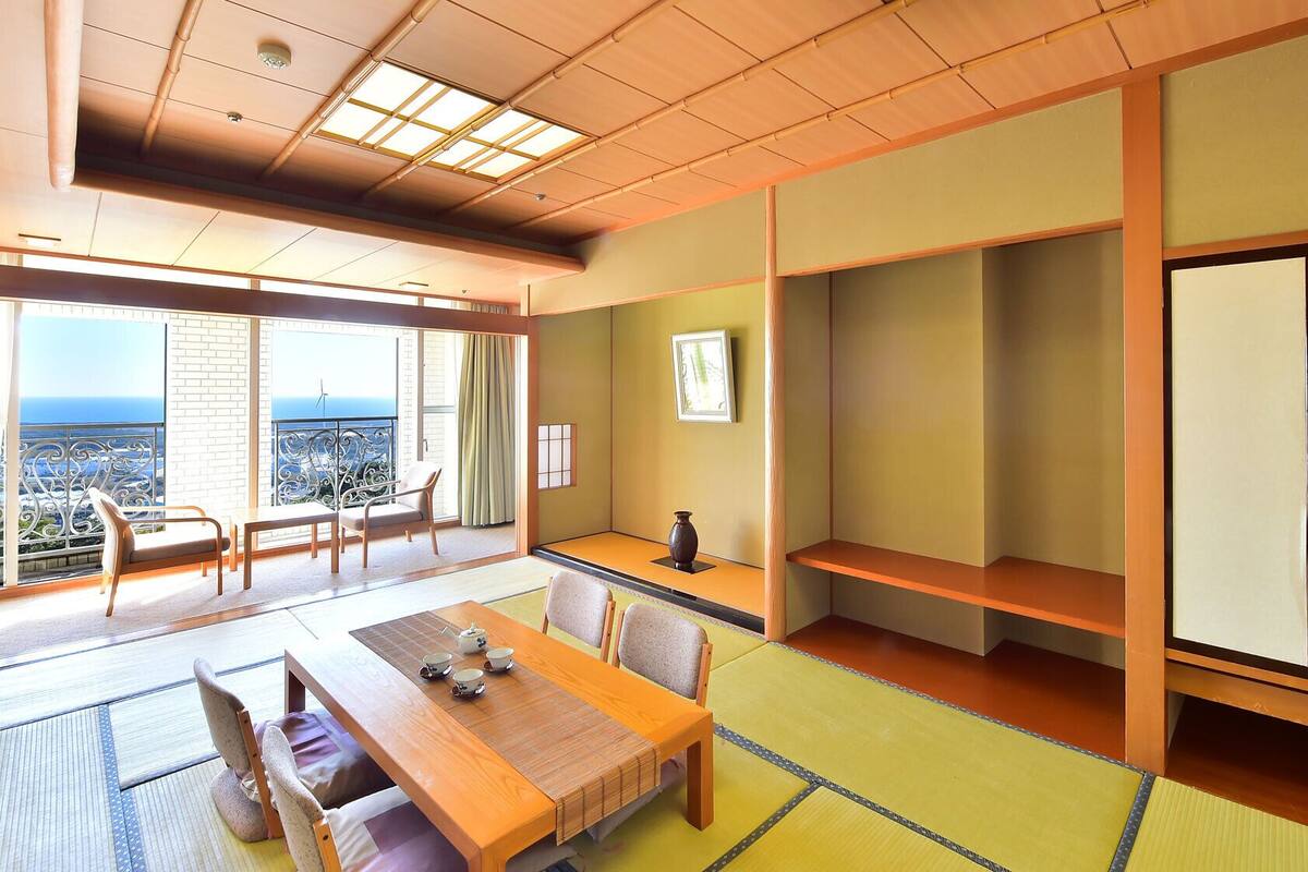 Una habitación tradicional japonesa con suelo de tatami, una mesa de madera baja con juego de té y vistas al mar a través de amplios ventanales.