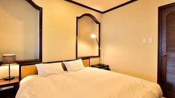 A hotel room with a large bed, a nightstand with a lamp, a mirror, and a door.