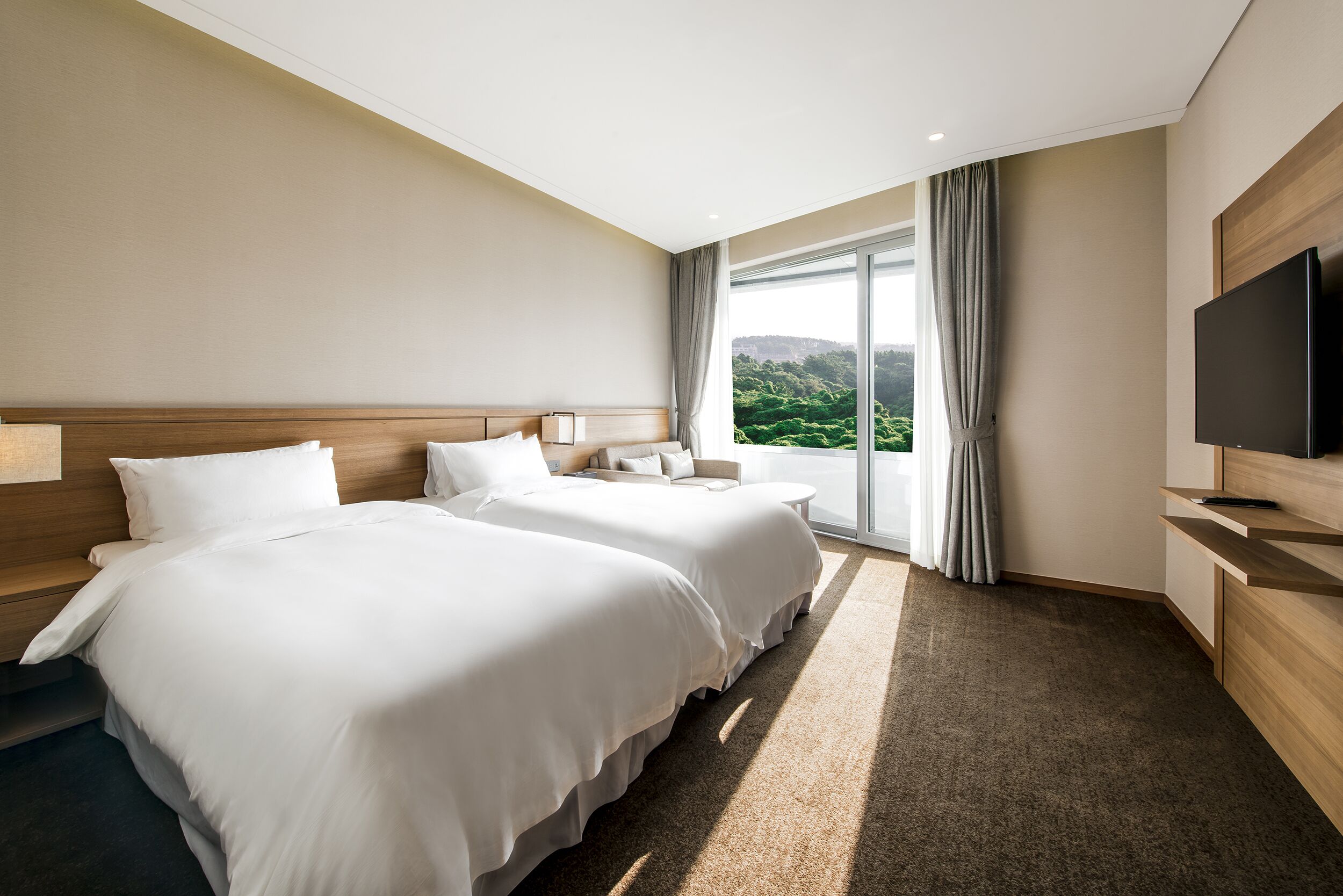 Quarto de hotel com duas camas, televisão, janela com cortinas e vista para área verde.