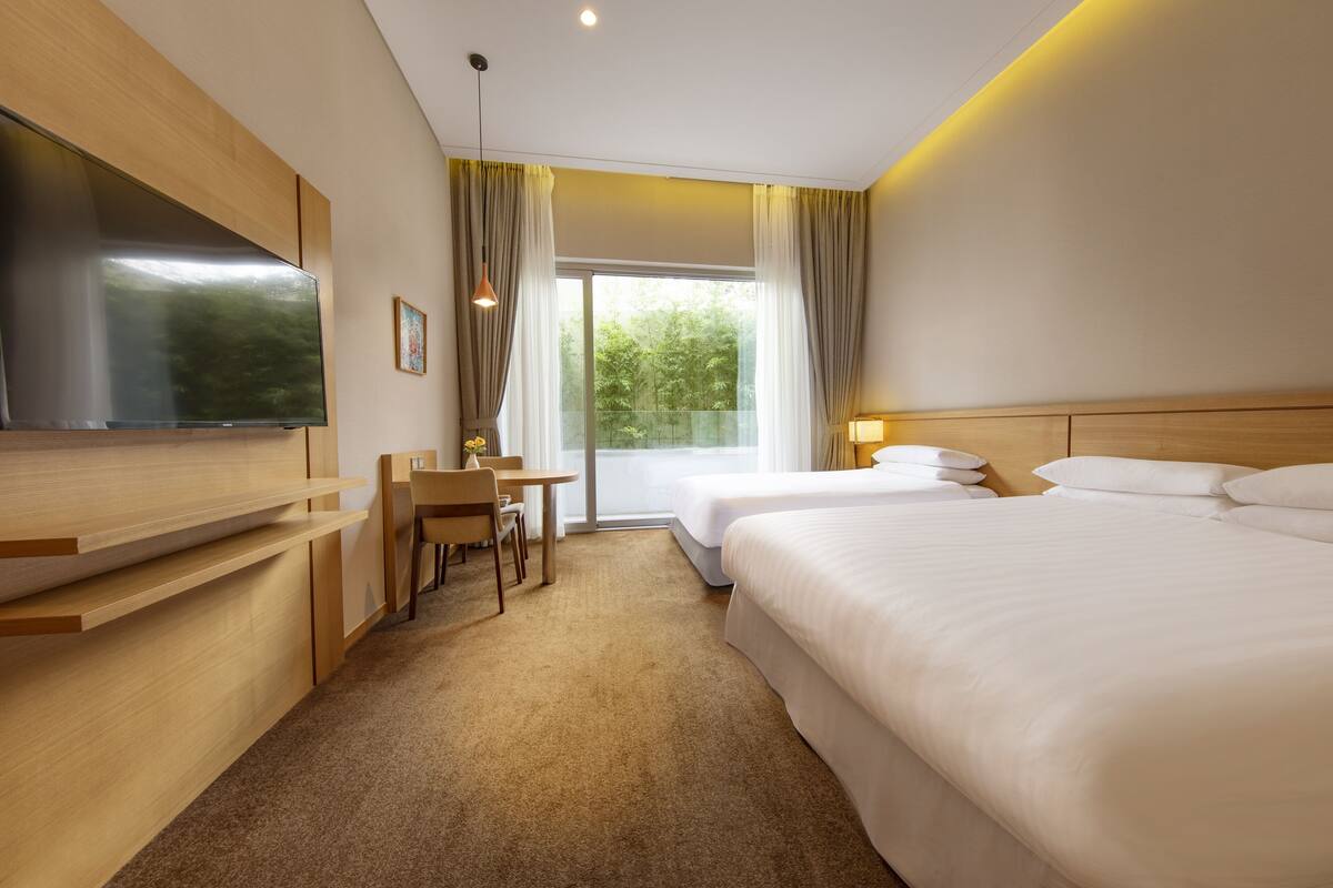 A hotel room with a bed, a desk, a chair, a TV, and a window with curtains.