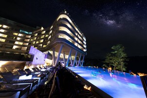 A modern hotel with a pool area at night, featuring a curved architecture and a view of the Milky Way.