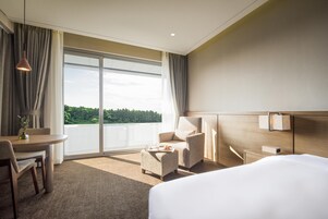 Una habitación de hotel moderna con una cama grande, un escritorio con una silla, un pequeño sofá y vistas a zonas verdes por la ventana.