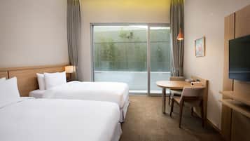 A hotel room with two beds, a small table with a chair, a TV, and a sliding glass door to the outside.