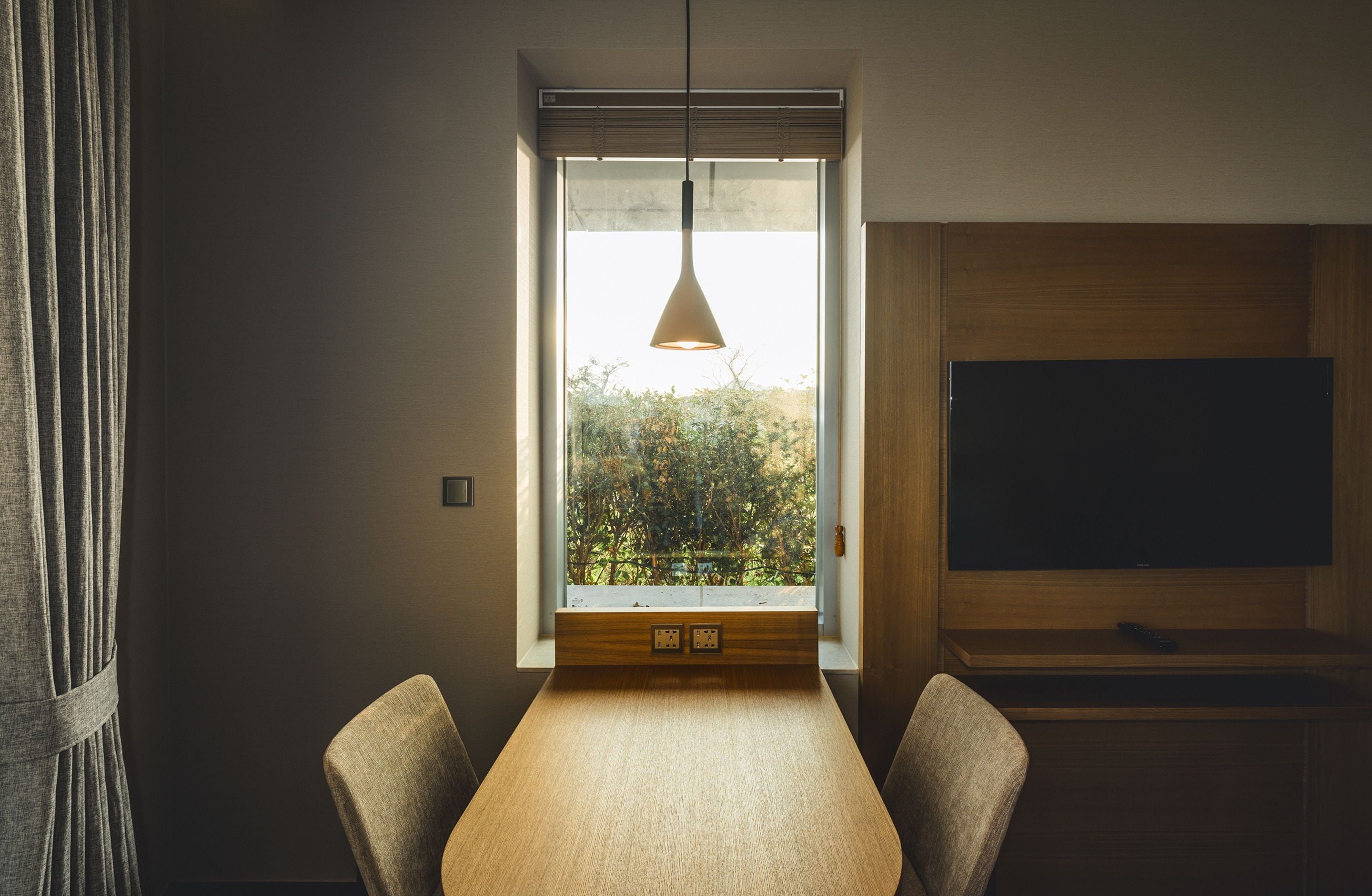 Ett modernt matområde med ett stort fönster, en hängande taklampa och en platt-TV som är monterad på väggen.