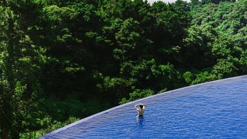 A person standing in a large, clear blue pool with a forested hillside in the background.