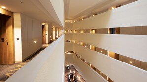 Et moderne hotelinteriør med en central atriumgård, flere etager og en lang gang med døre på venstre side.