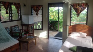 A room with a bed, a small table, a chair, a television, and a view of the outdoors. - Tiavi Mountain Cabins (Siumu)