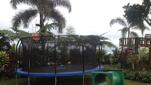 A trampoline with a safety net, surrounded by lush greenery and palm trees. - Tiavi Mountain Cabins (Siumu)