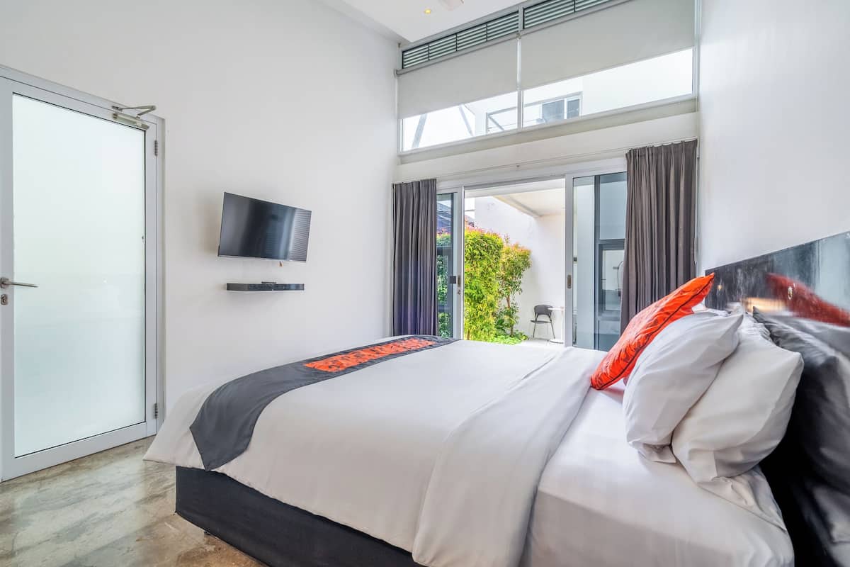 A modern hotel room with a large bed, a flat-screen TV, and a balcony with curtains.