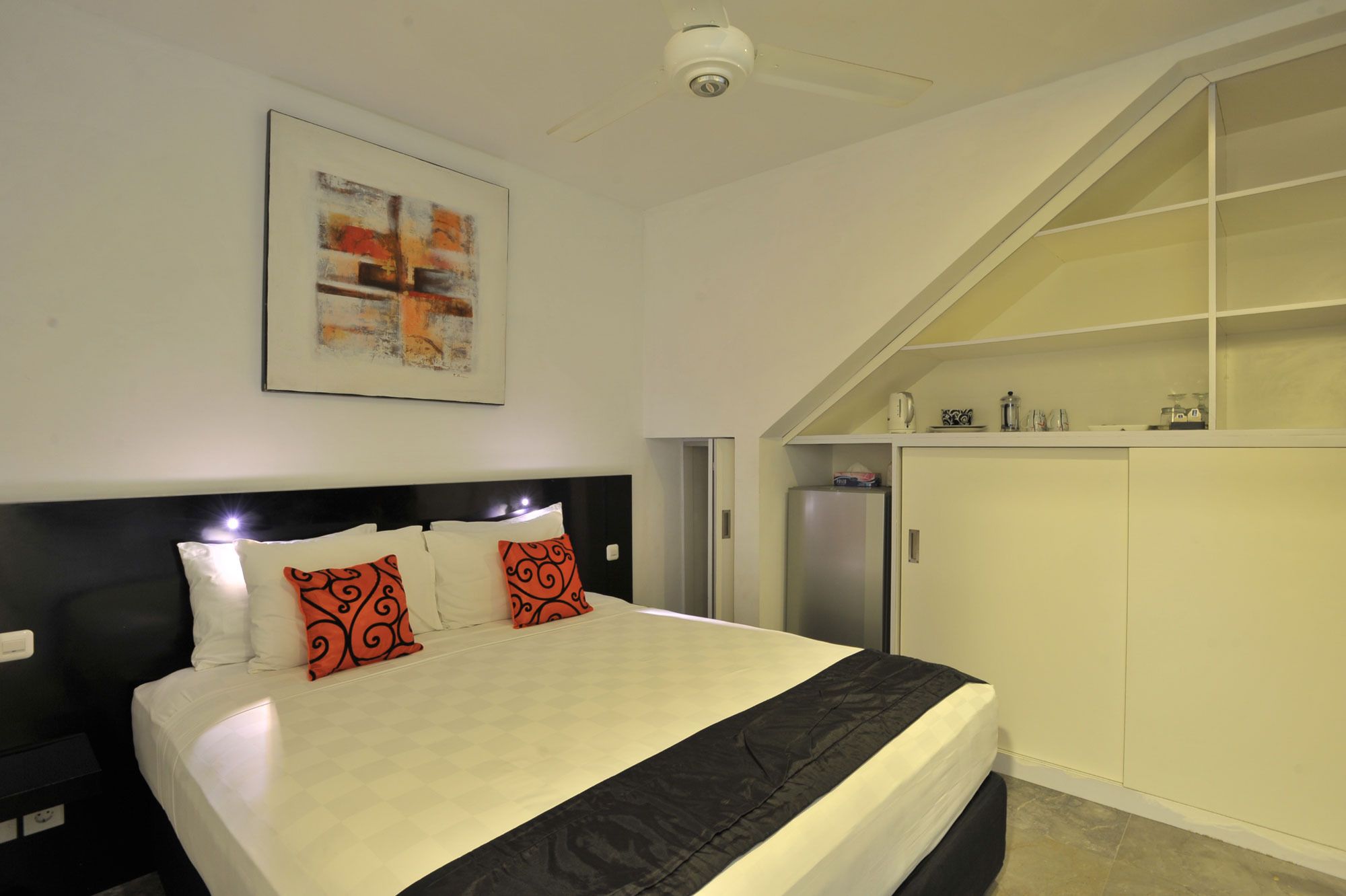 Une chambre à coucher comprenant un lit, une tête de lit, une œuvre d’art accrochée au mur, une armoire et un ventilateur de plafond.