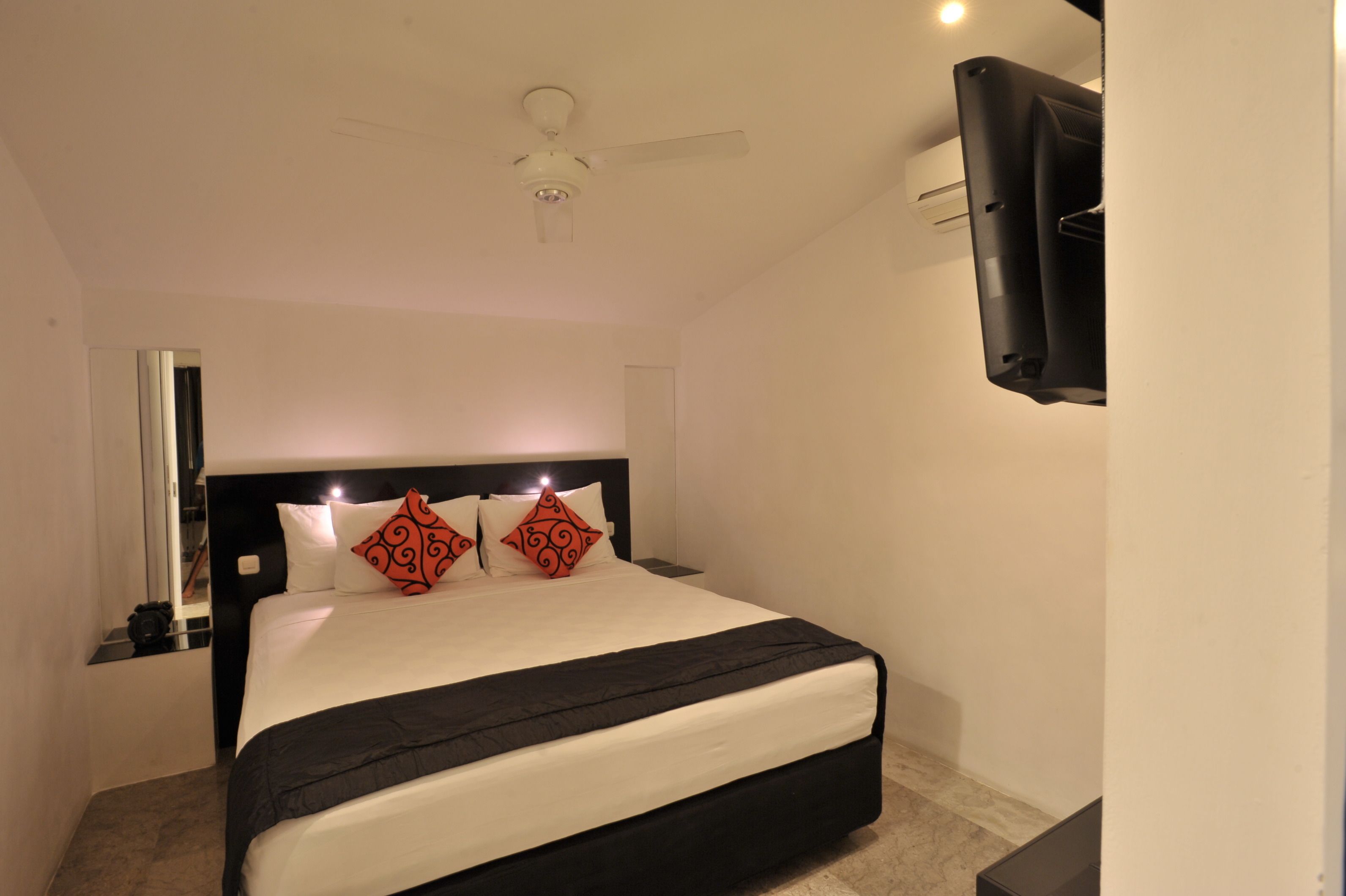 A hotel room with a bed, a ceiling fan, a TV mounted on the wall, and a nightstand.