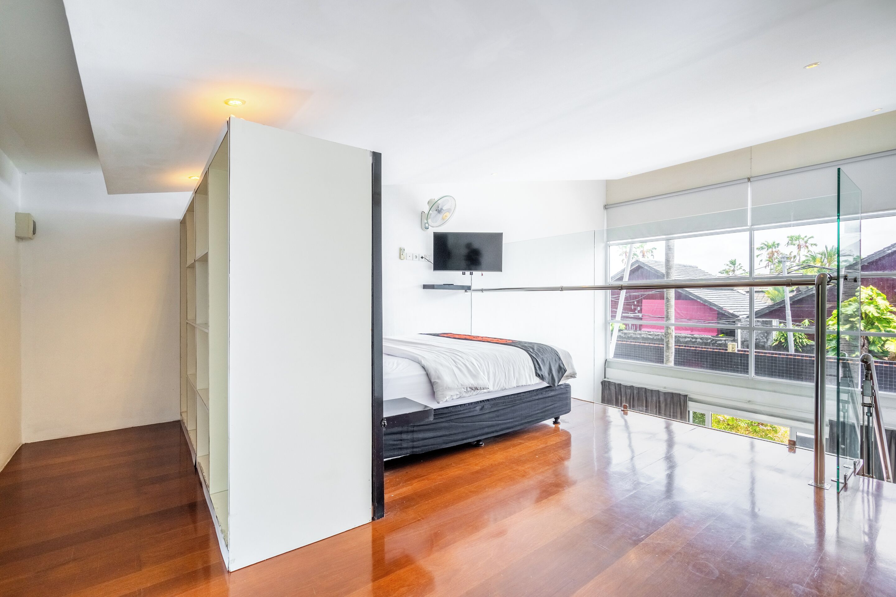 A modern bedroom with a bed, a TV, and a large window with a view of palm trees and houses.