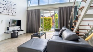 A modern living room with a large window, a flat-screen TV, a sofa, and a staircase. - Bali Yarra Villas Seminyak (Seminyak)