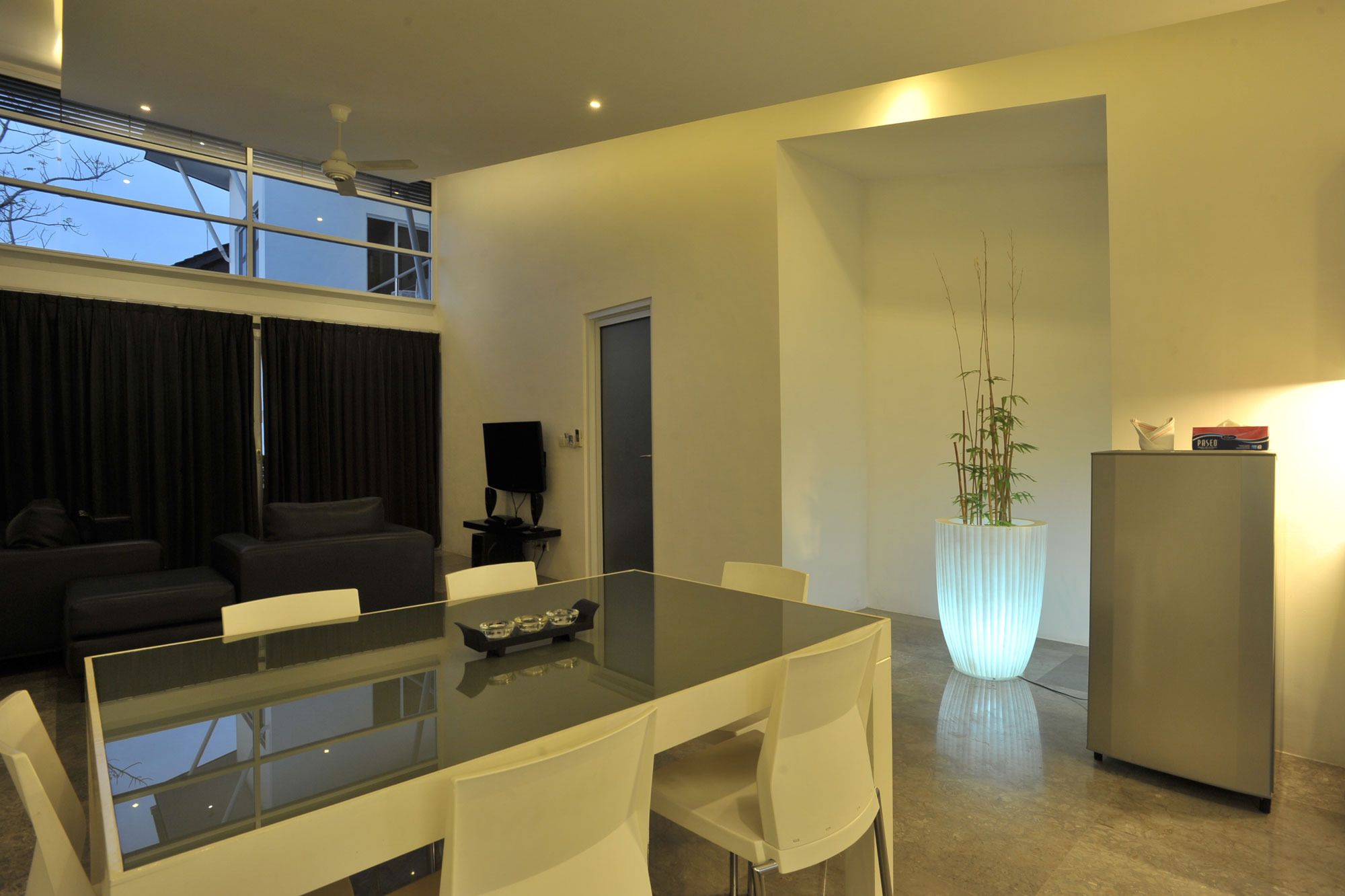A modern living room with a glass dining table, white chairs, a sofa, and a large window.