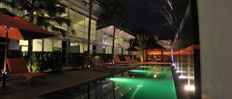 A nighttime pool area with lounge chairs and a building in the background.
