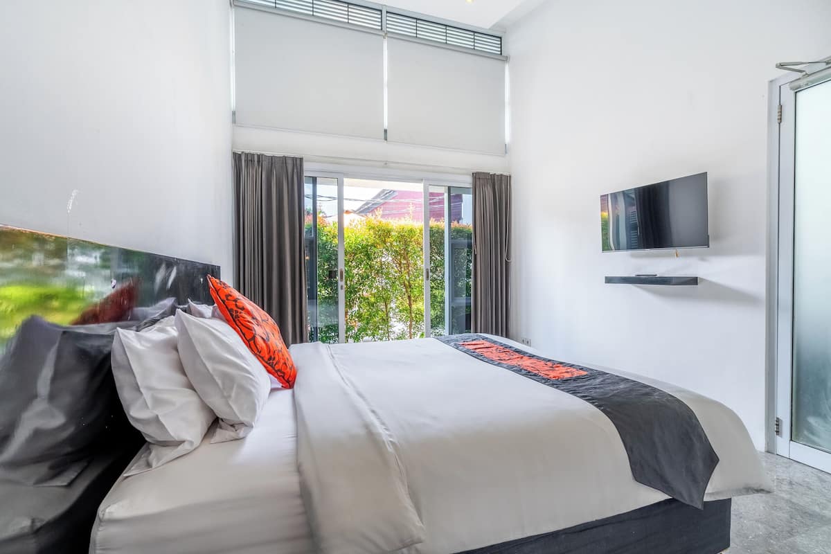 A modern hotel room with a large bed, a flat-screen TV, and a view of greenery through the window.