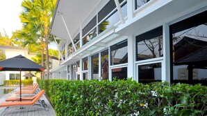 A modern building with large windows, a pool area with lounge chairs, and a well-maintained hedge. - Bali Yarra Villas Seminyak (Seminyak)