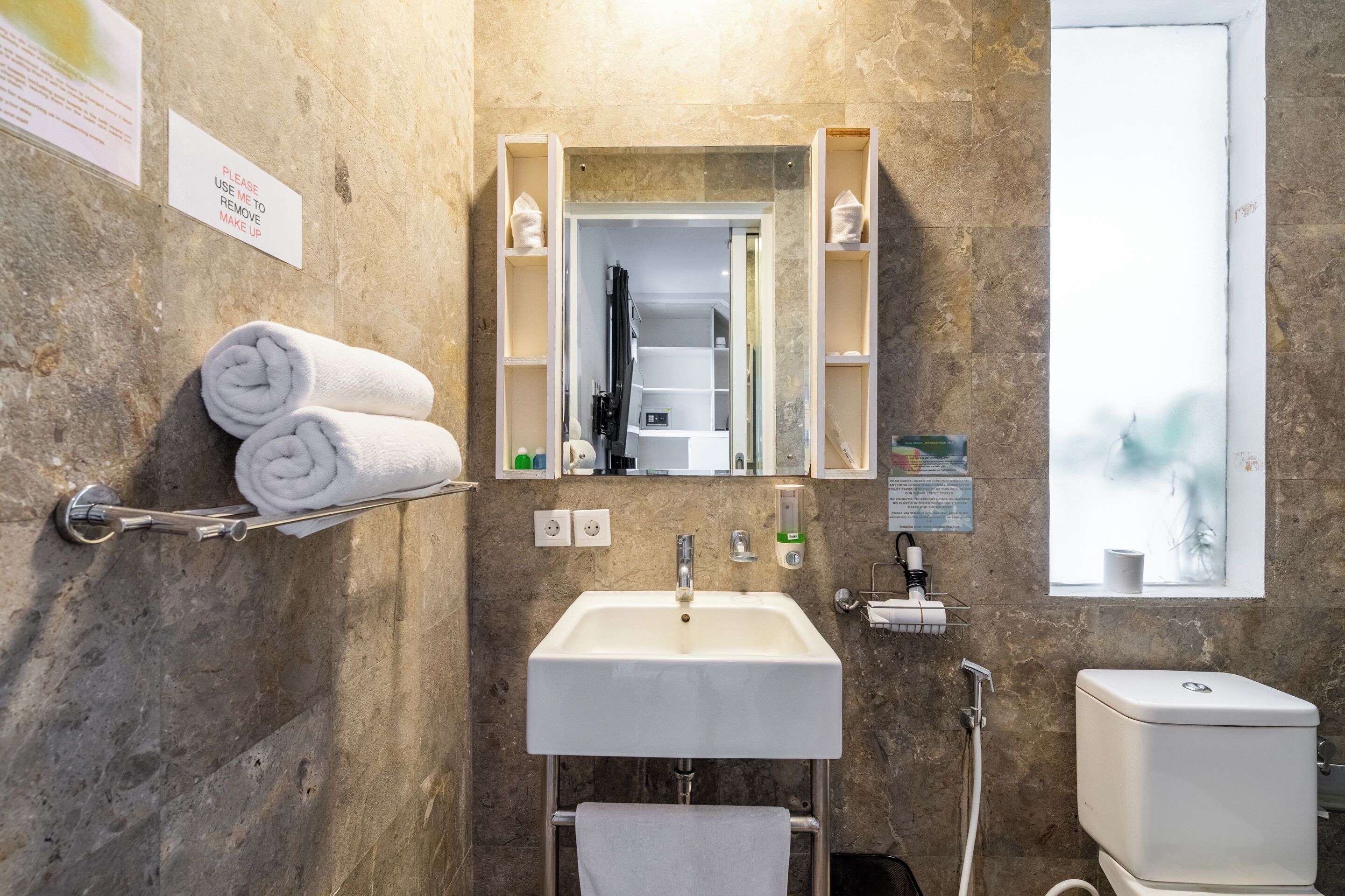 Ein Badezimmer mit Marmorwand, einem weißen Waschbecken, einer Toilette und einem Handtuchhalter mit gerollten Handtüchern.