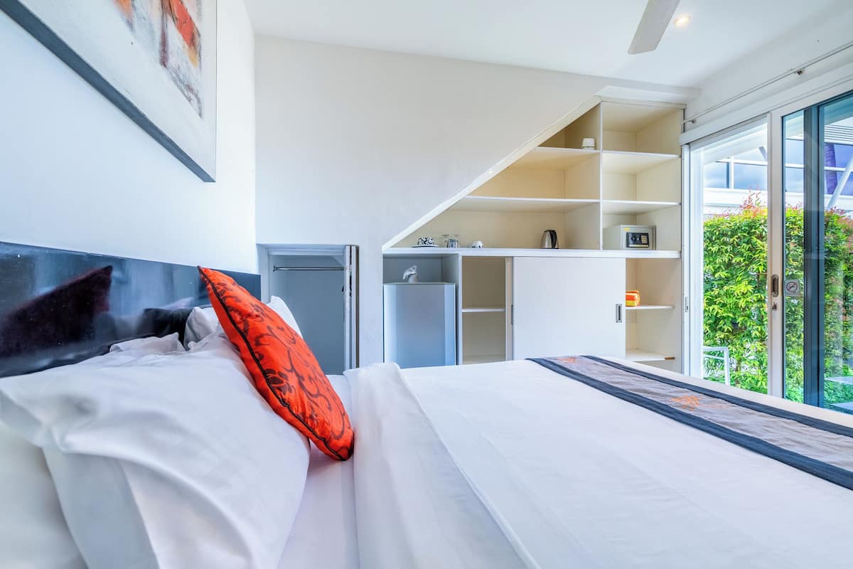 A modern hotel room with a large bed, a built-in wardrobe, a small kitchenette, and a sliding glass door to the outside.