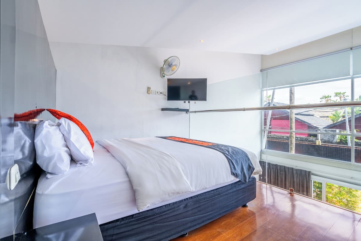 A modern bedroom with a large bed, a flat-screen TV mounted on the wall, and a large window offering a view of the outside.