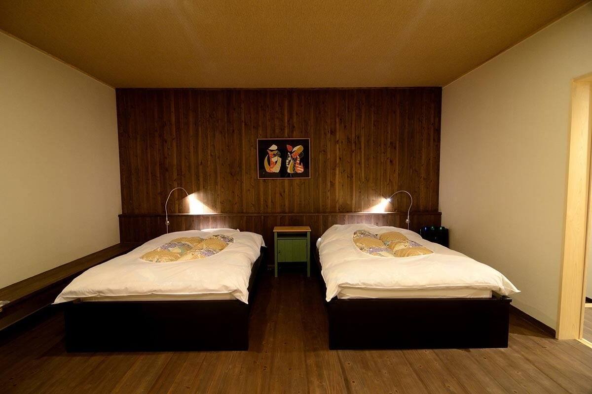 A room with two beds, wooden walls, and a small table between them.