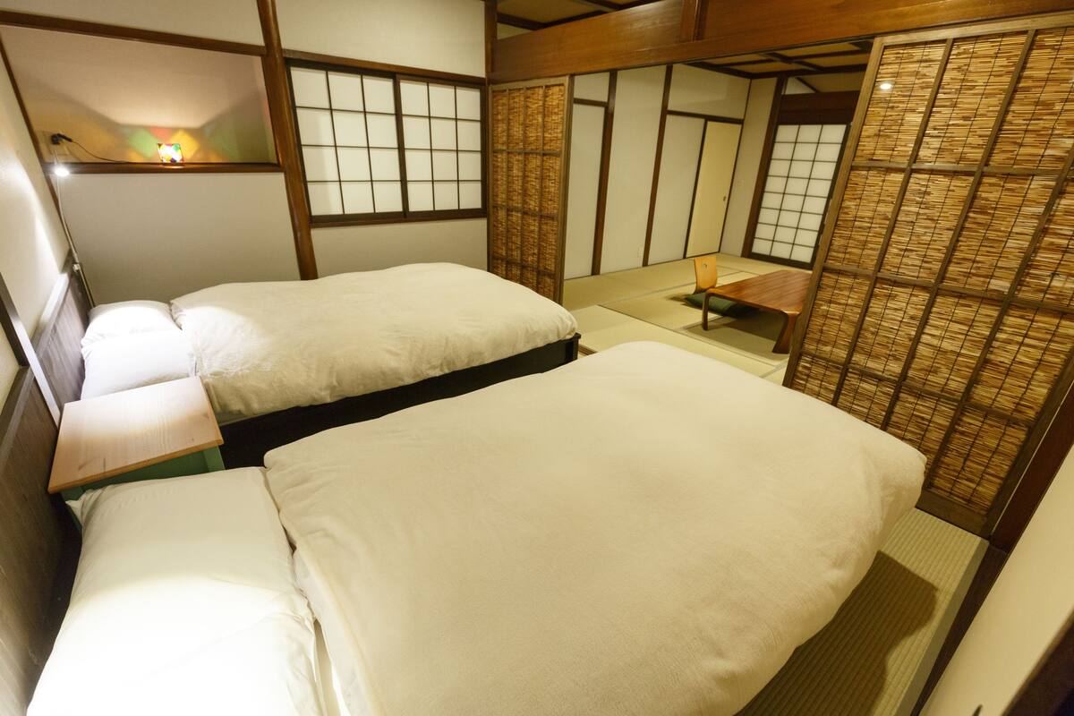 A traditional Japanese-style room with two beds, tatami flooring, shoji screens, and a small table.
