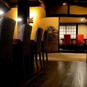 A dining area with wooden chairs and a table, a plant, and a view through a sliding door.
