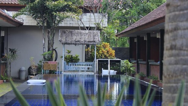 An infinity pool with a thatched structure in the background, surrounded by lush greenery and a small white fence. - Puri Ganesh Hotel (Legian)