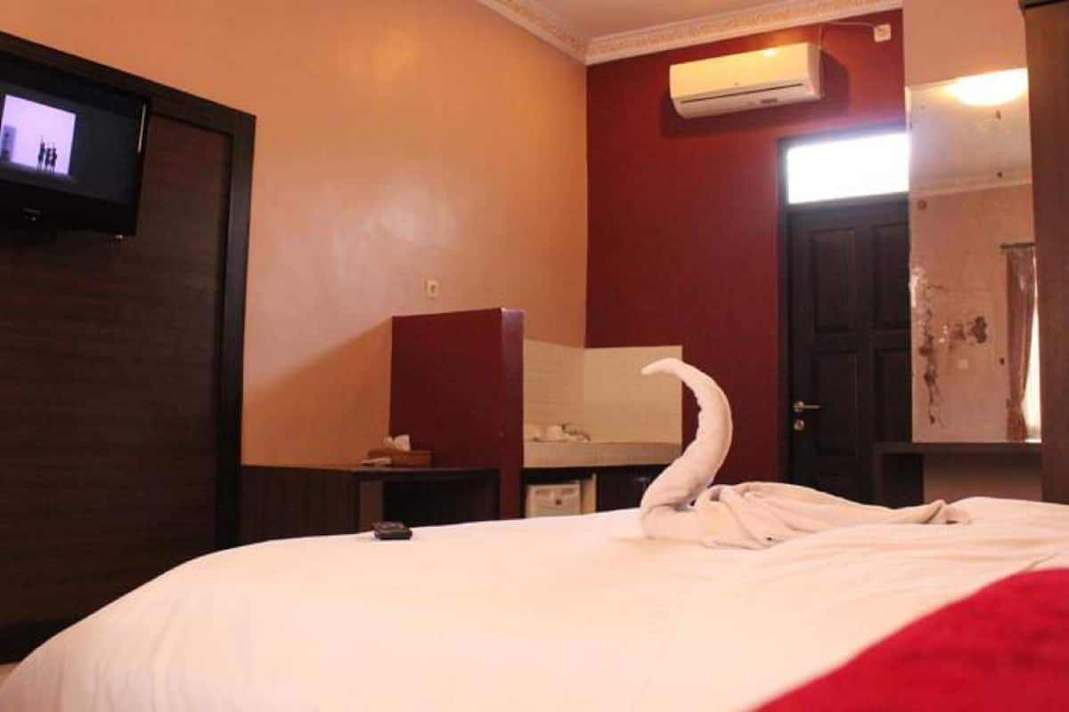A hotel room with a bed, a television on the wall, an air conditioning unit, and a mirror.