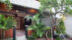 A courtyard with a brick pathway, potted plants, and a stone wall. - Puri Ganesh Hotel (Legian)